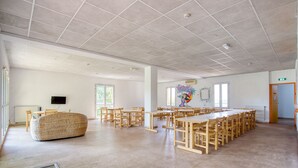 A spacious room with a long table and chairs, a bean bag, and a television on the wall. - Auberge de Fréjus Saint-Raphael - Hostel (Fréjus)