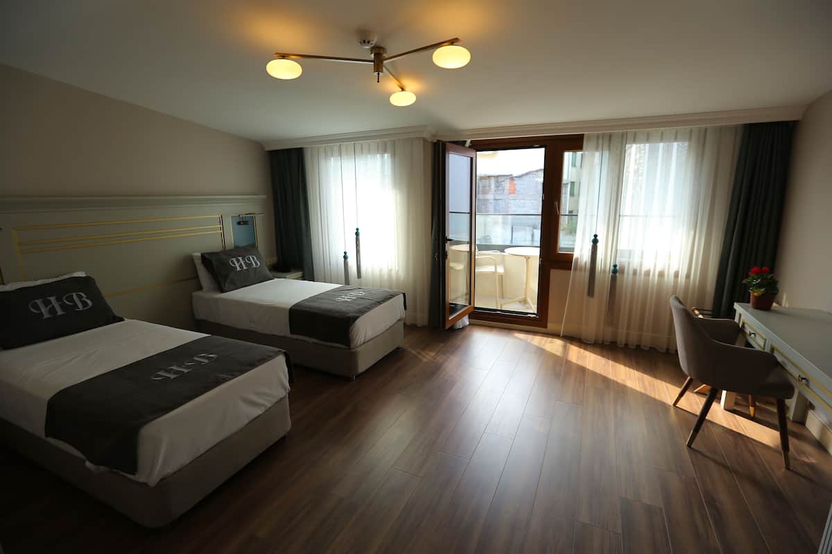 A hotel room with two beds, a desk, a chair, and a balcony with a view.