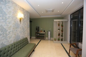 A room with a green sofa, a small table with a lamp, a cabinet with potted plants, and a sliding glass door.