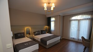 A hotel room with two beds, a chandelier, a nightstand, a chair, and a large window with curtains. - Haci Bayram Hotel (Istanbul)