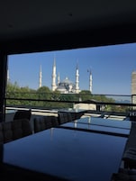 A view of a mosque with multiple minarets from a modern building with a glass table and chairs.