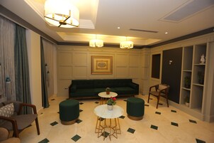 Un salón moderno con un sofá verde, dos mesas redondas con plantas en macetas y una lámpara decorativa en el techo.