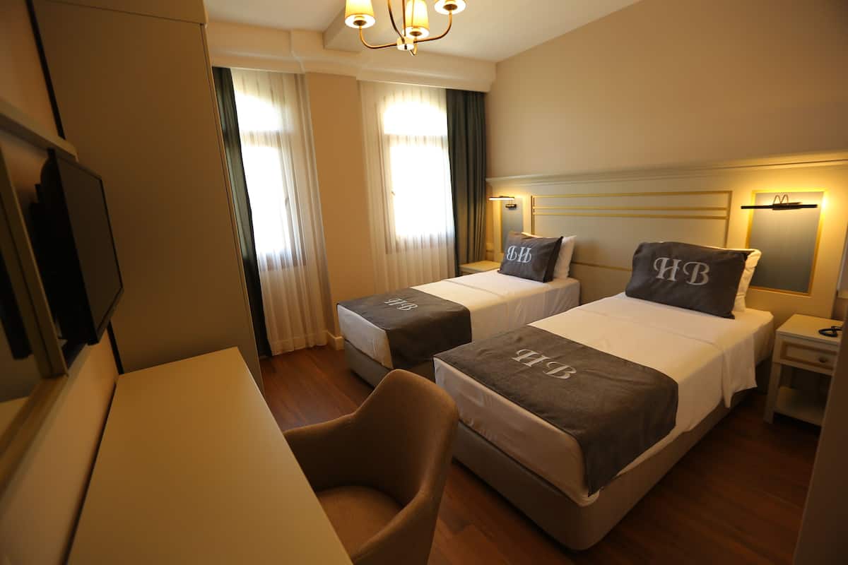 A hotel room with two beds, a desk, a chair, and a television.