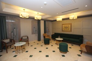 Un área de descanso moderna con un sofá verde, sillas de madera, una mesa redonda y lámparas decorativas.