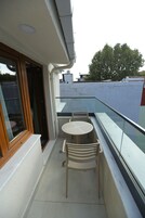 Ein Balkon mit Tisch und Stühlen, ein Fenster und Blick auf Himmel und Bäume.