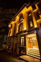 Un edificio de varios pisos con una entrada bien iluminada, ventanas amplias y una escalera visible que conduce a la entrada.