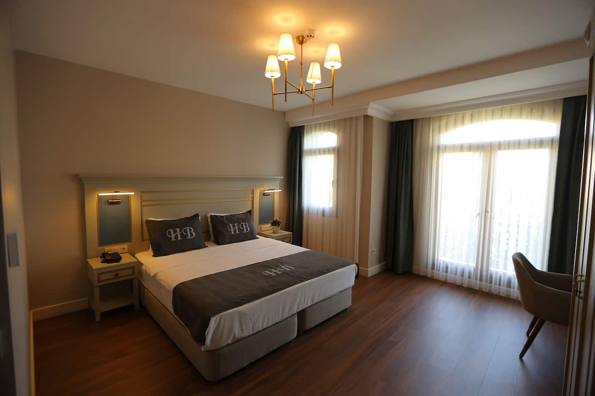 A hotel room with a large bed, bedside tables, a chair, and a chandelier.