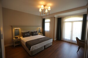 A hotel room with a large bed, bedside tables, a chair, and a chandelier.
