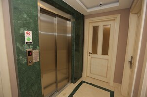 Un ascensor con un panel de control digital, una pared de mármol verde y una puerta color beige con un panel de vidrio.