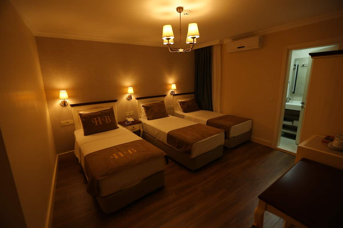 A hotel room with two beds, a desk, and a chair. There are bedside lamps and a ceiling light.
