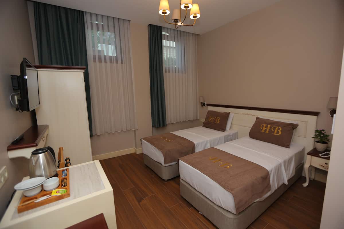 A hotel room with two single beds, a desk with a coffee maker, a TV, and a small table with a tray of breakfast items.