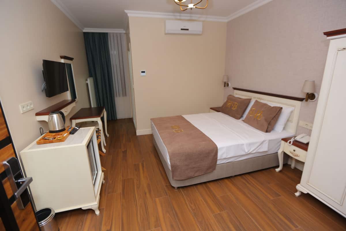 A hotel room with a bed, bedside table, TV, and a small kitchenette.