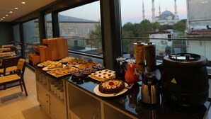 A breakfast buffet with a variety of pastries and cakes, a coffee machine, and a view of a mosque with minarets in the background. - Haci Bayram Hotel (Istanbul)