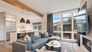 Een moderne woonkamer met een grijze bank, een open haard en een groot raam met uitzicht op een schilderachtige omgeving.