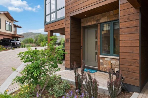 Una casa moderna de dos pisos con fachada de madera, un muro de acento de piedra y un camino de entrada con coches estacionados.