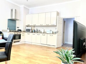 A modern kitchen with white cabinets, a microwave, a stove, and a large flat-screen TV.