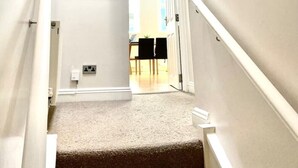 A narrow, carpeted stairway with white walls and a wooden-framed mirror. - Sight Flat - SF01 - One Bedroom Flat (London)