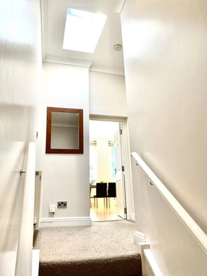 A narrow, carpeted stairway with white walls and a wooden-framed mirror.