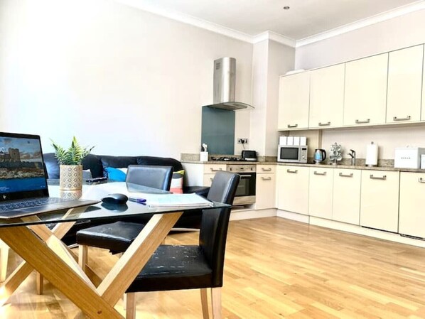 A modern kitchen with white cabinets, a microwave, and a stove. There is a dining area with a table and chairs, and a laptop on the table.