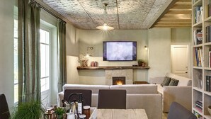 A cozy living room with a fireplace, a television mounted above it, and a bookshelf filled with books. - Olimagio Farmstay w/animals & 25m pool <4km Forte dei Marmi beach (Pietrasanta)