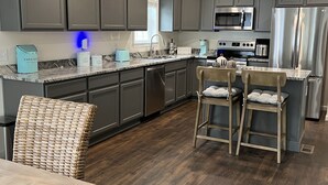 A modern kitchen with grey cabinets, stainless steel appliances, and a wooden dining area. - Cozy New Home, Close to Beaches, Restaurants and Bike Trials, Free EV charging  (Rehoboth Beach)
