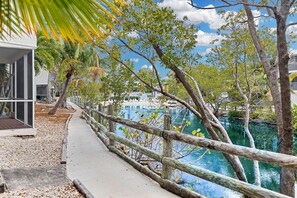 A pathway leading to a body of water with a wooden railing, surrounded by trees and a modern building. - Turtle Tavern @ Kawama Yacht Club (Key Largo)