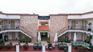 Un edificio con un letrero que dice 'JLAN CUNDA NONNA', que presenta una escalera central, asientos exteriores con mesas y sillas, y plantas en macetas.