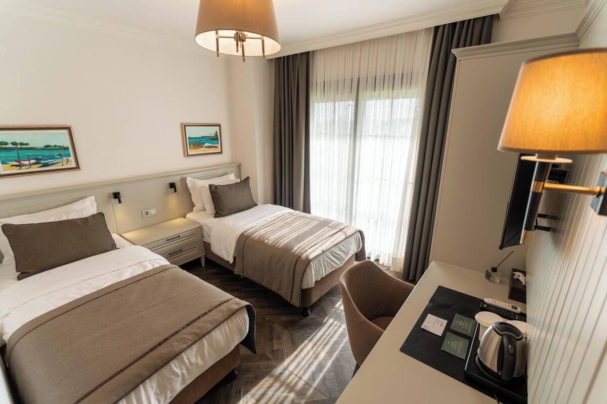 Een hotelkamer met twee bedden, een bureau met een waterkoker, een stoel en een televisie.