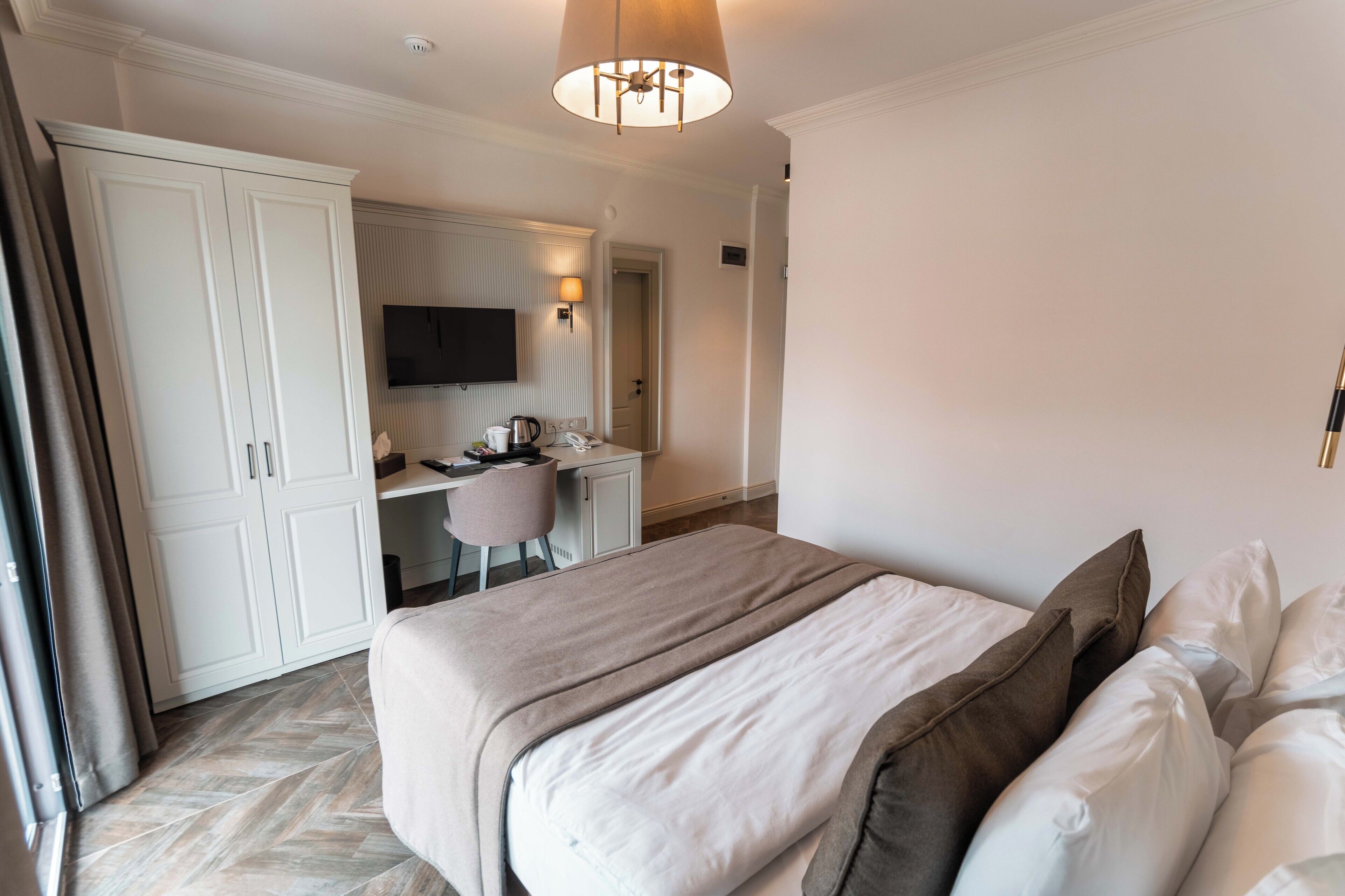 A hotel room with a bed, a desk, a chair, a television, and a wardrobe.