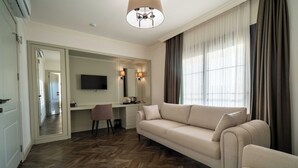 Habitación de hotel con sofá, escritorio con televisor de pantalla plana, silla y ventana grande con cortinas.