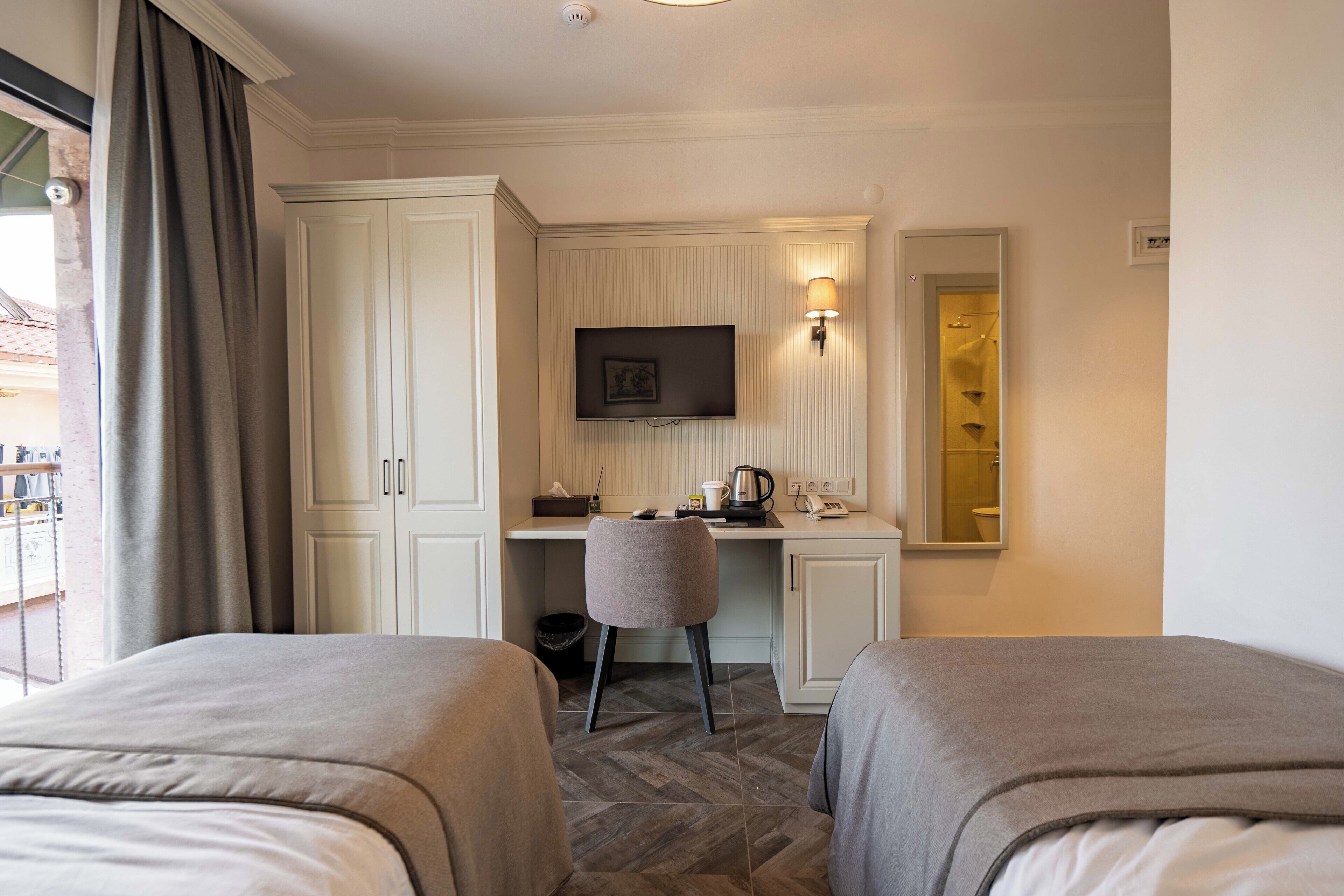 A hotel room with two beds, a desk with a chair, a television, and a mirror.