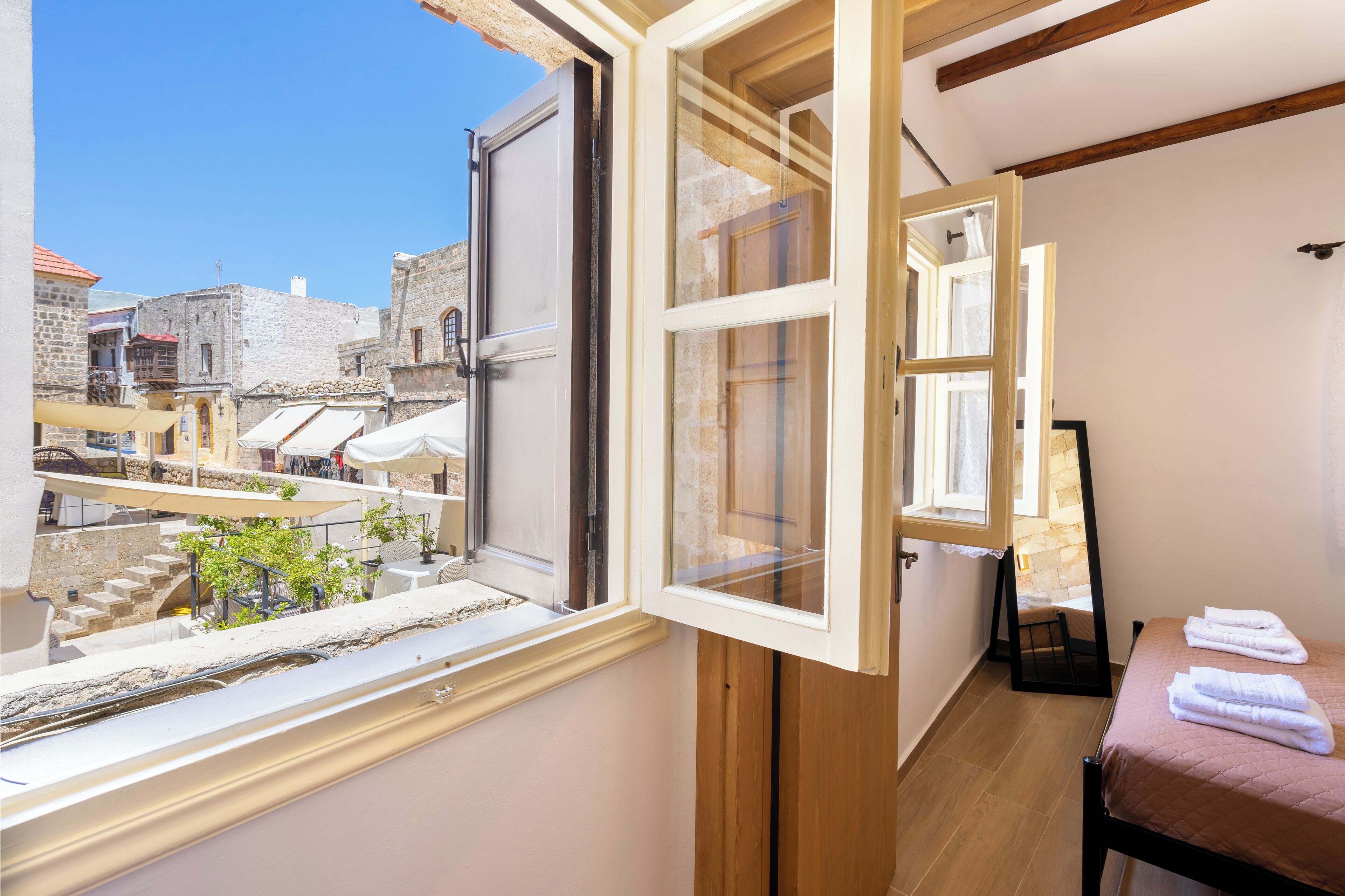 A room with a large window, a bed, a wooden floor, and a view of a historic town.