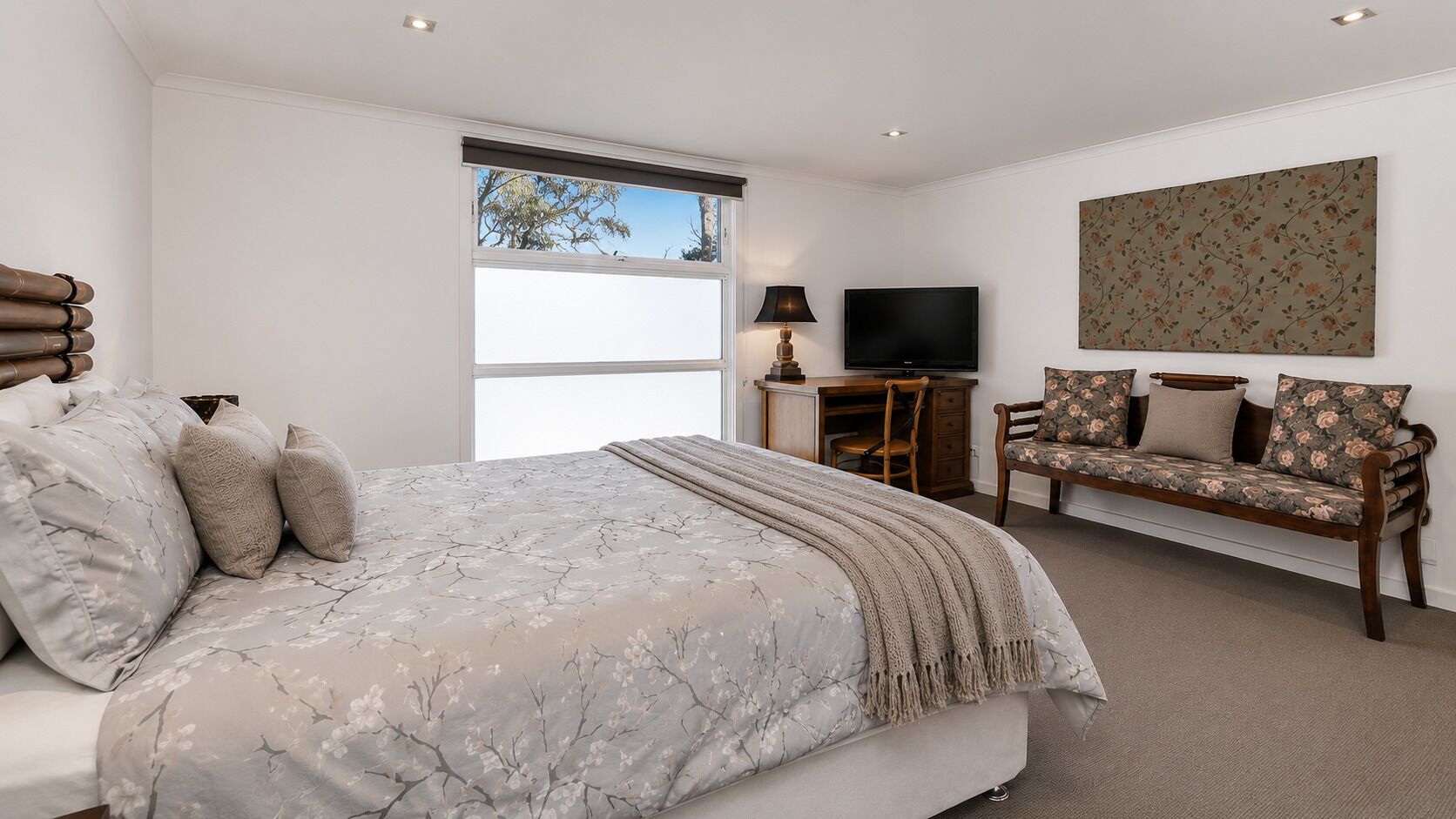 A bedroom with a bed, a sofa, a television, and a window.