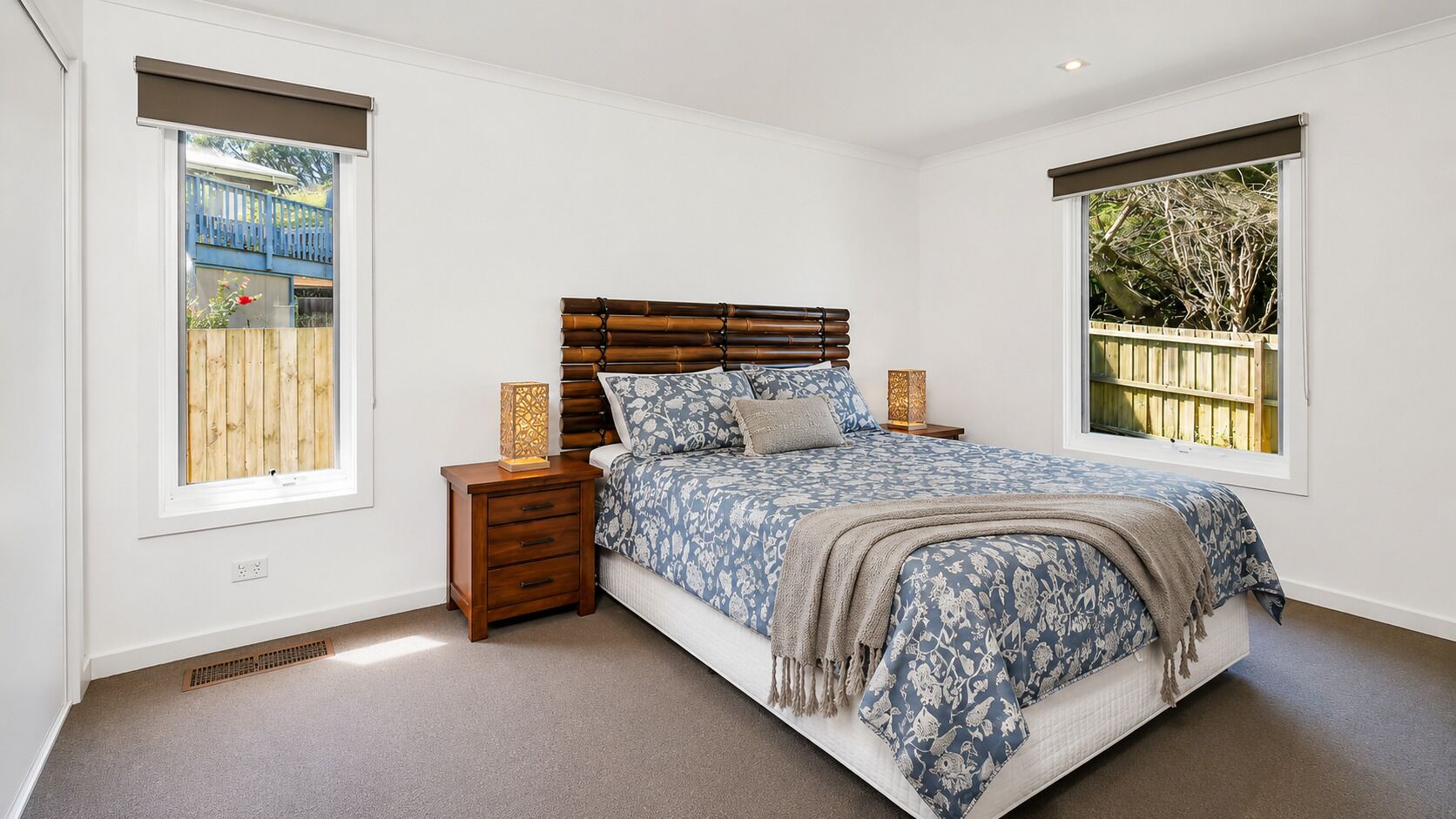 Une chambre à coucher avec un grand lit, une table de chevet, une lampe de chevet et une fenêtre donnant sur une clôture en bois.