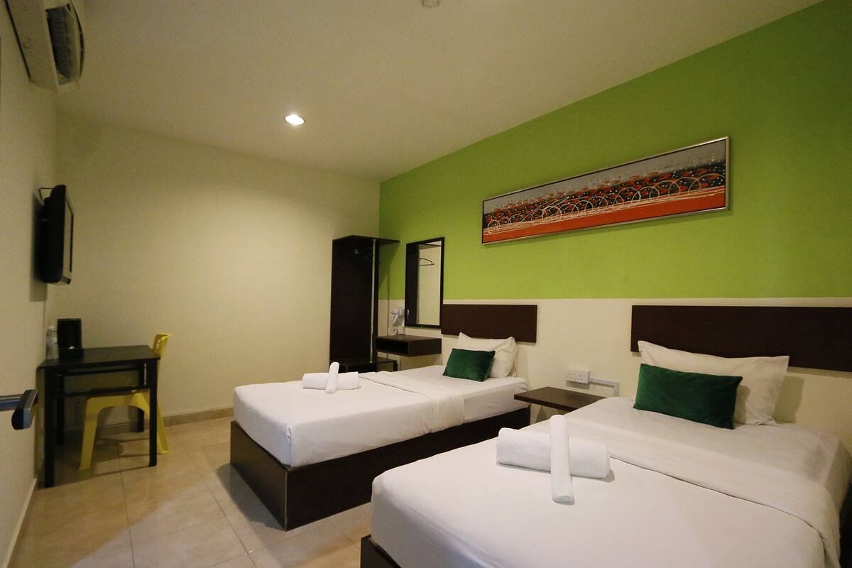 A hotel room with two beds, a desk, a chair, a TV, and a painting on the wall.