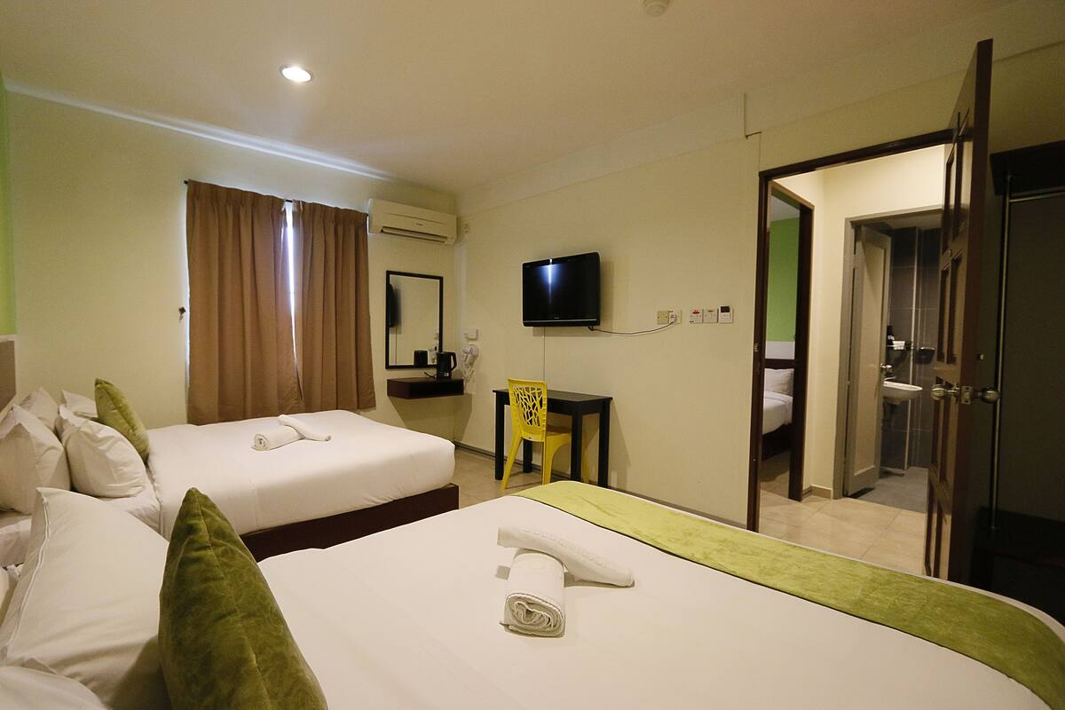 A hotel room with two beds, a television, a desk, and a bathroom visible through an open door.