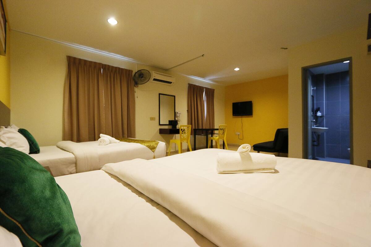 A hotel room with two beds, a desk, a chair, a television, and a bathroom visible through an open door.