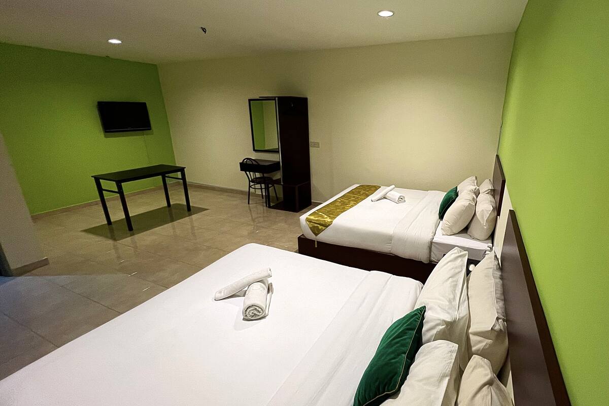 A hotel room with two beds, a desk, a chair, and a TV on the wall.
