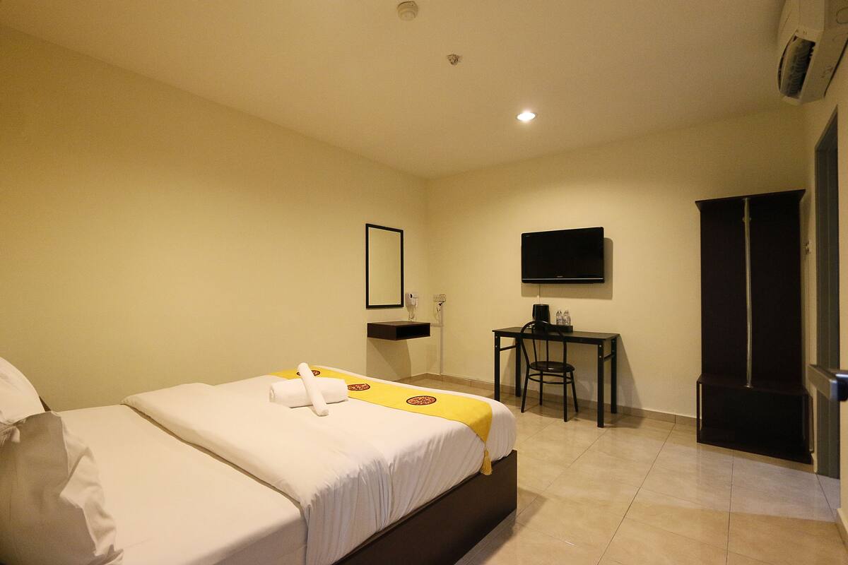 A hotel room with a bed, a desk, a chair, a television, and a wardrobe.