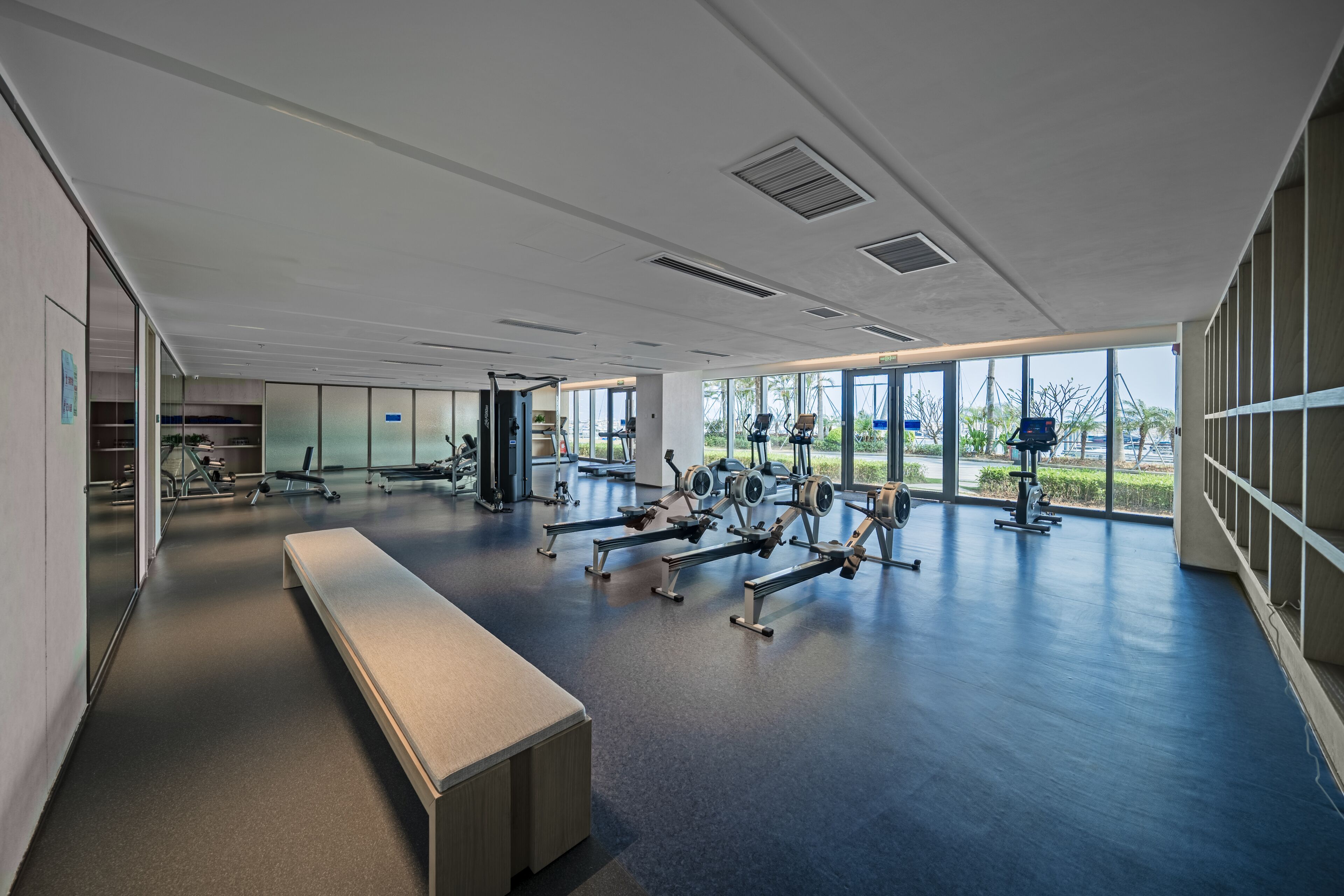Een moderne sportschool met trainingsapparatuur, grote ramen en een bank.