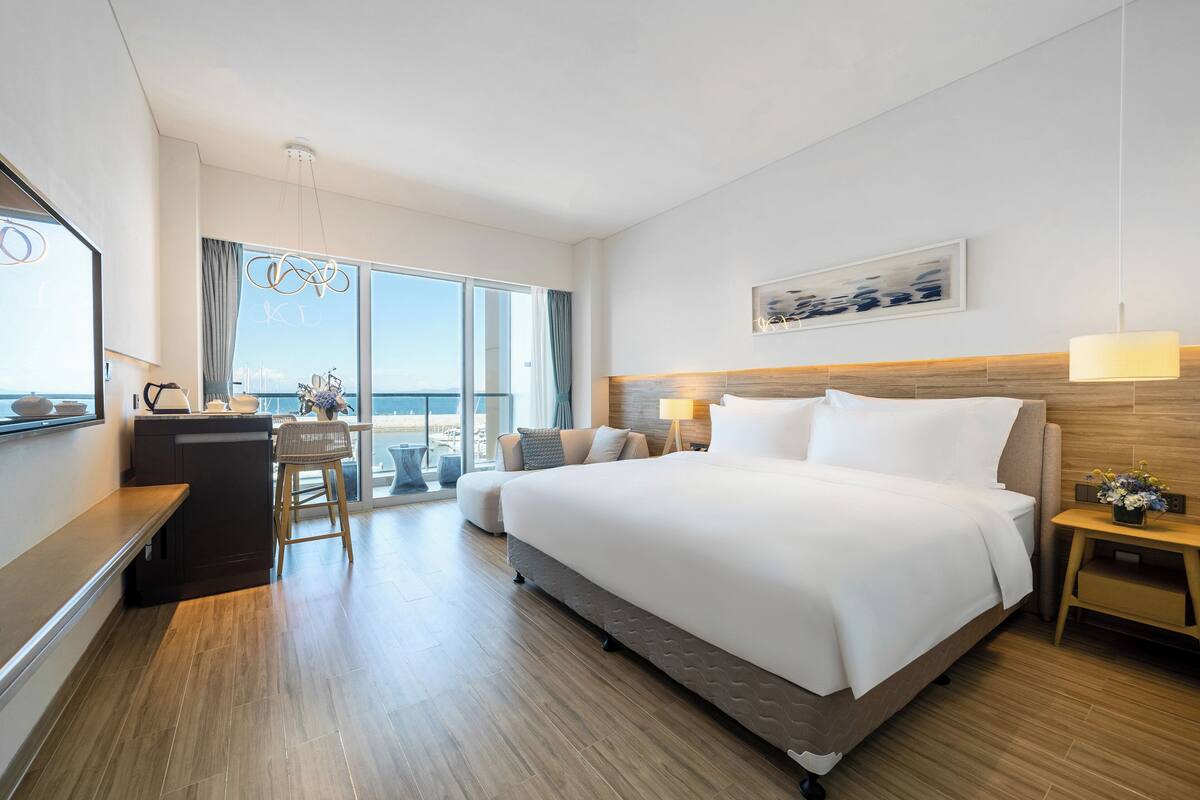 Habitación de hotel moderna con una cama grande, un escritorio, una silla y vista al océano.