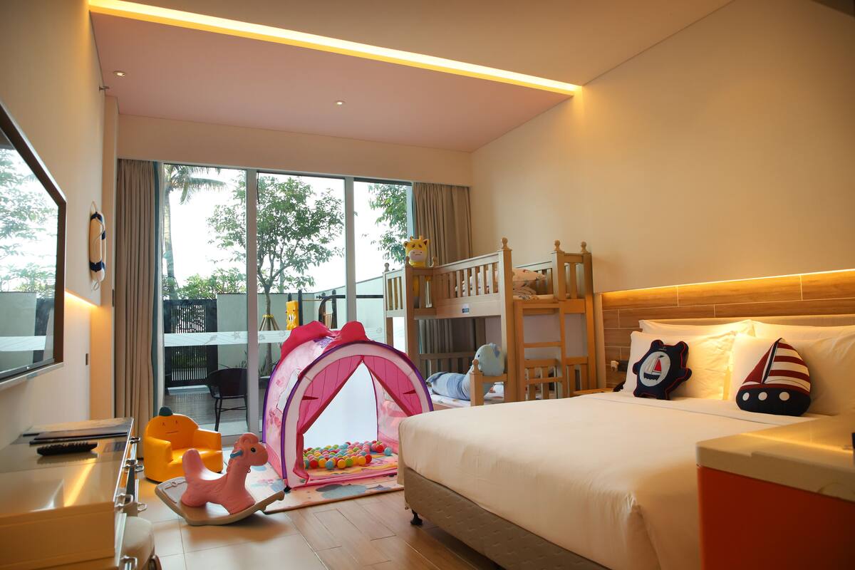 Habitación de hotel con cama, una tienda de juegos, un caballo de juguete y vistas al exterior.