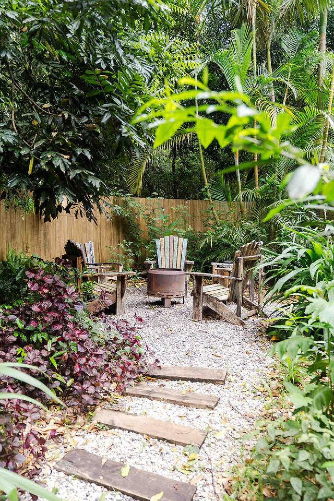 A garden with a fire pit, wooden chairs, and a gravel path.