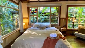 A bedroom with a large bed, wooden beams, a ceiling fan, and large windows with a view of greenery. - Ananda Eco House - Rainforest Retreat (Montville)
