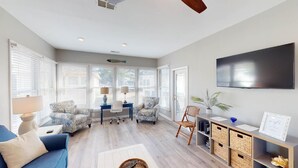 A spacious living room with a large TV, comfortable seating, and a view through the glass door.
