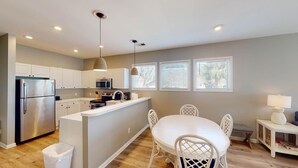 A modern kitchen with white cabinetry, a stainless steel refrigerator, a microwave, and a coffee maker. There is a dining area with a white table and chairs.