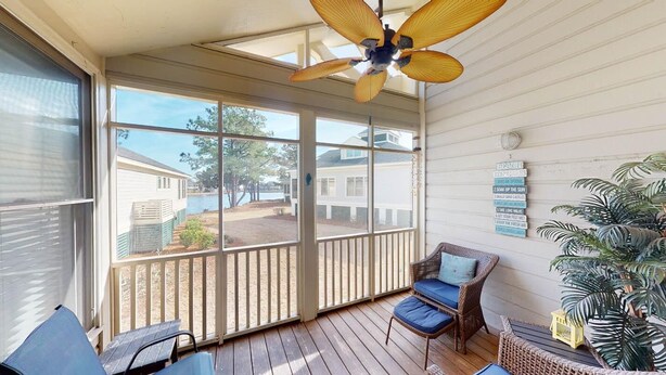 A covered porch with a ceiling fan, wicker furniture, and a view of a lake and houses.