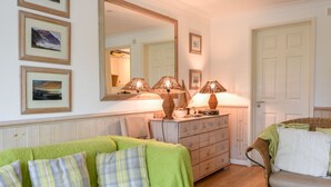 Una habitación acogedora con un sofá verde, un sillón de mimbre, un aparador con lámparas y cuadros en la pared.