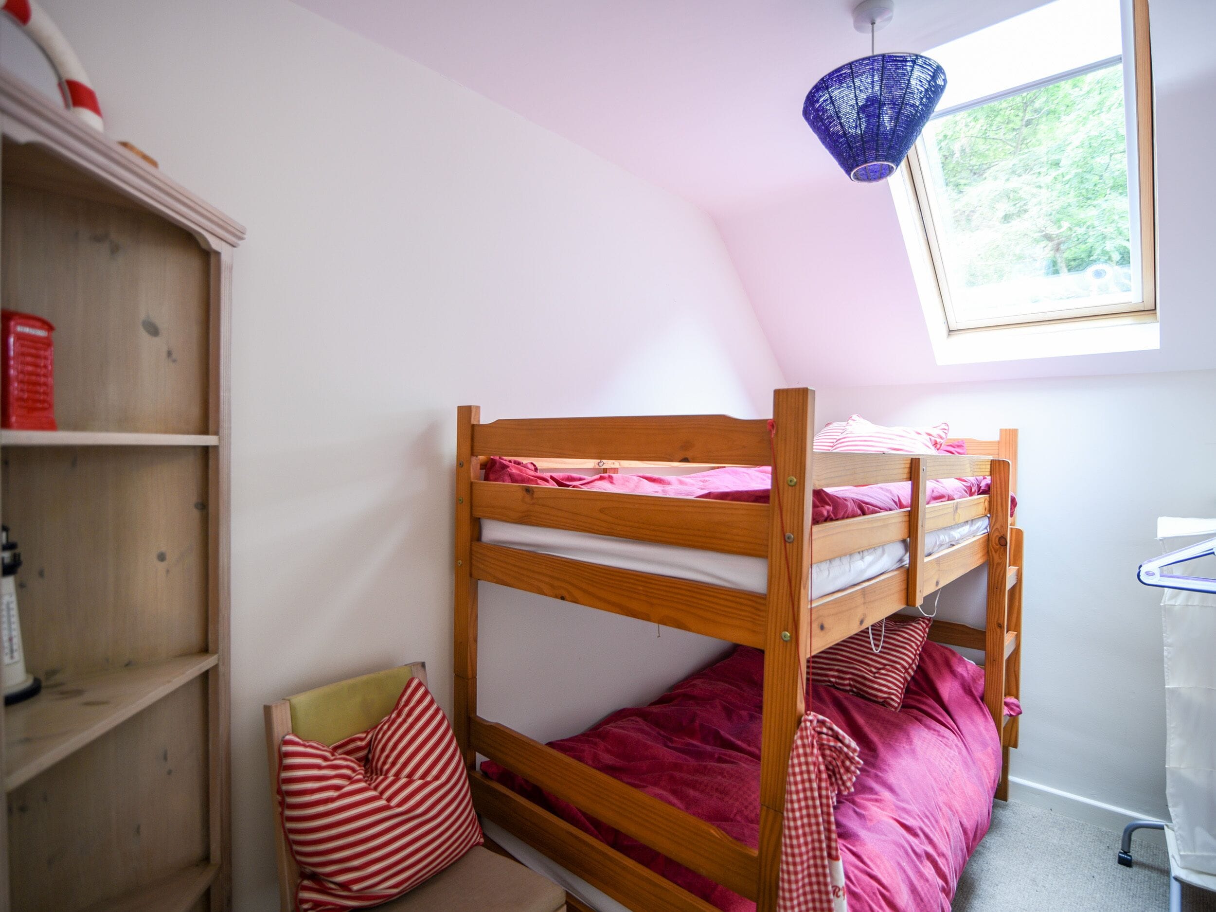 A small, well-lit room with a bunk bed, a wooden shelf with books, and a skylight.
