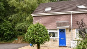 Una casa de dos pisos con una puerta azul, un pequeño jardín y un árbol al frente.